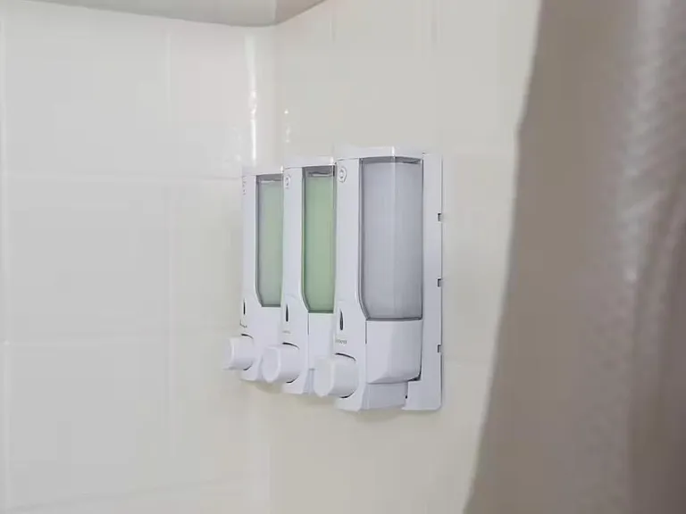 Shower area with tiled surround and convenient mounted dispensers for soap, shampoo, and conditioner.