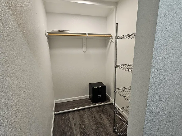 Walk-in closet with hanging rod, upper shelf, and freestanding wire shelving for organized storage.