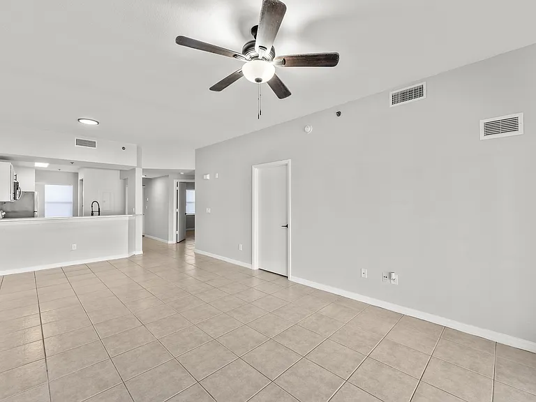 Bright, open-concept living area with tiled flooring and modern ceiling fan, leading into a sleek kitchen space.
