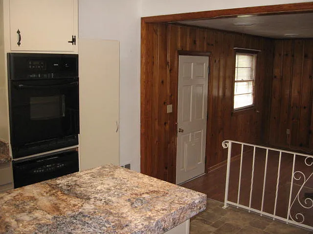 This picture shows the sunken family room which is open to the kitchen. The family room has a decorative fireplace. The wood paneling has been painted. The door showing opens to backyard. There is a door on the opposite wall that leads out to the garage.