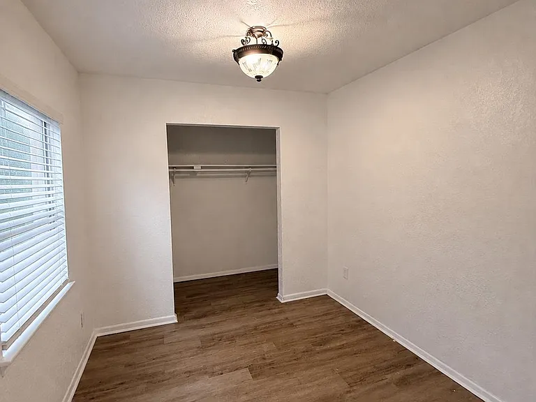 Unfurnished bedroom with wood-look flooring, a window with blinds, and an open closet for easy storage and organization.