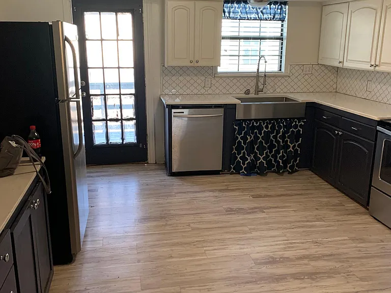 Kitchen has stainless refrigerator, dishwasher, and stove. It has white quartz countertops with white tile backsplash. Back exits to covered Bach porch.