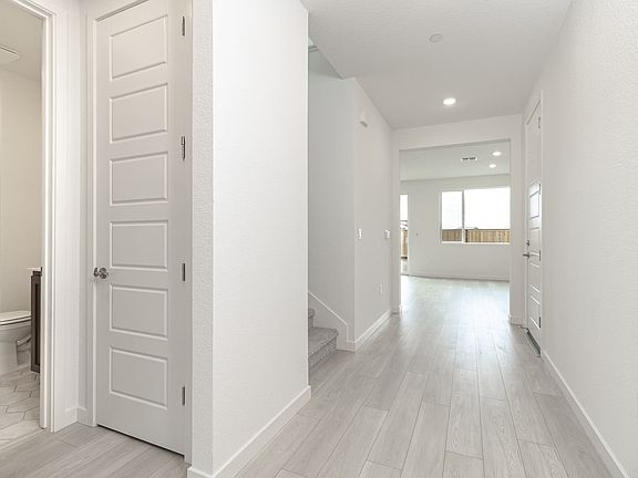 A bright, spacious hallway with white walls, a wooden floor, and a partially visible bathroom door.