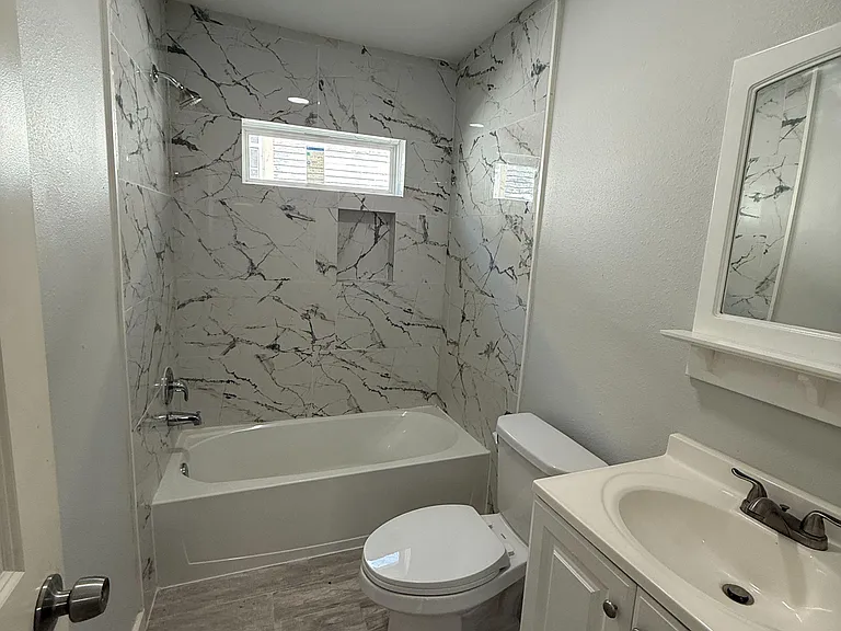 Updated full bathroom with tub/shower surround, vanity sink, and a window for ventilation and natural light.