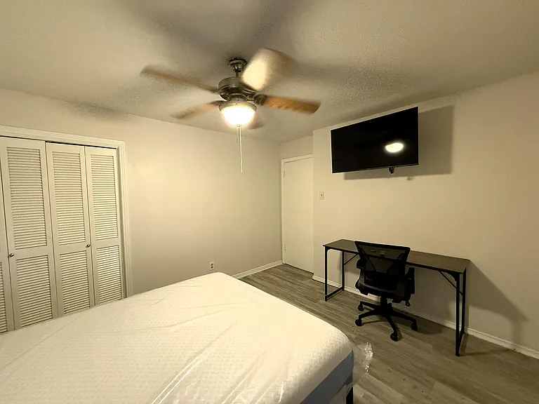 Furnished bedroom with ceiling fan, wall-mounted TV, large closet, and dedicated desk space for work or study.