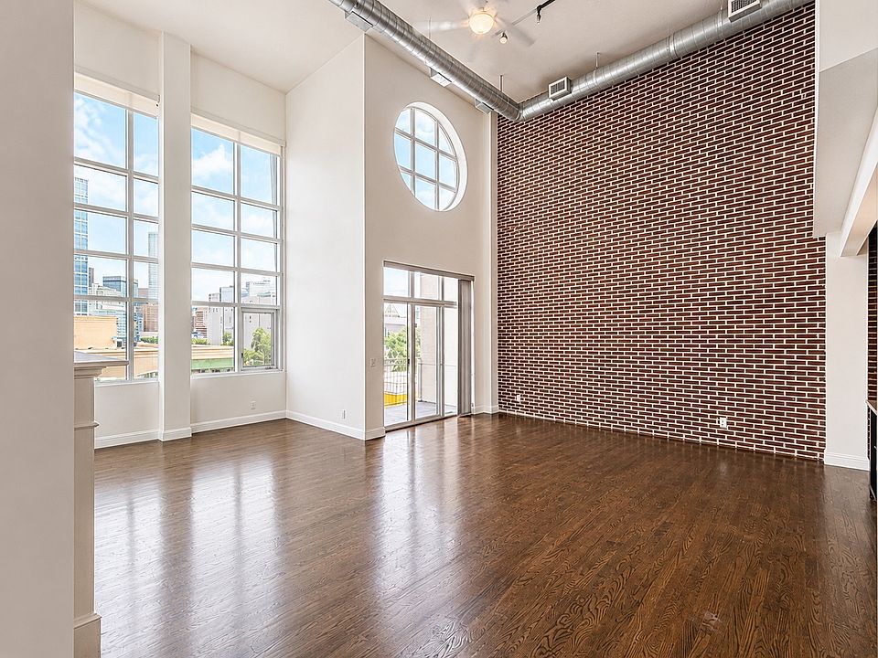 Dramatic living room with 20-foot ceilings, exposed brick, oversized windows, and private balcony access.