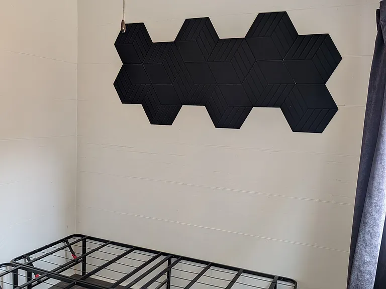 Bedroom with full-sized bed frame and sound-dampening wall panels. Bedroom also has its own ceiling fan.