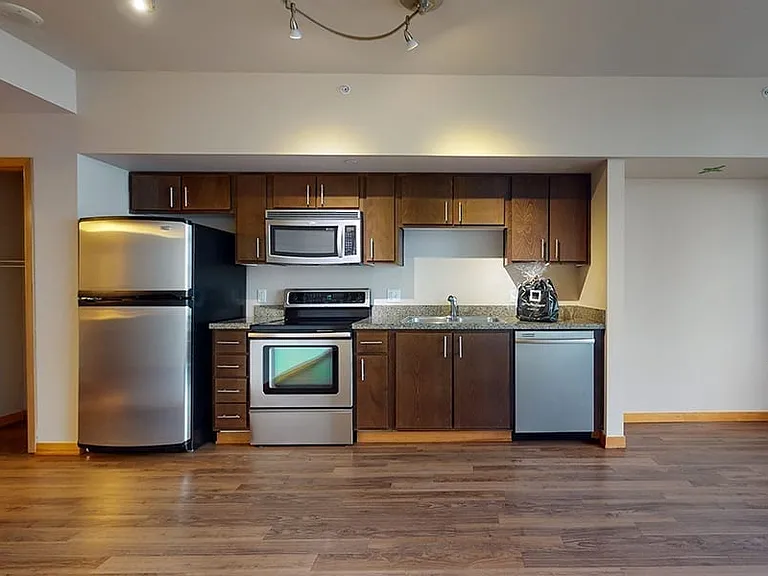 Apartment kitchen with stainless steel appliances, granite countertops and wood-style flooring.