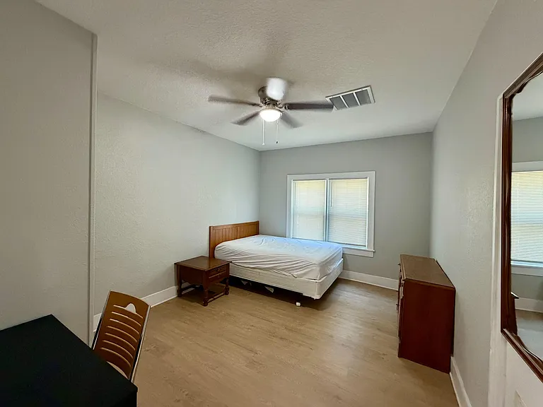 Furnished bedroom with a ceiling fan, wood-style flooring, and a window with blinds, plus dresser and nightstand storage.