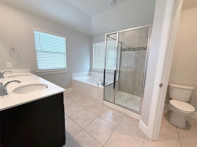 Spa-inspired primary bathroom featuring a dual-sink vanity with white quartz countertop, frameless glass shower enclosure with tile surround, soaking tub, and neutral tile flooring throughout