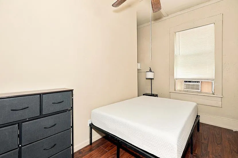 Furnished bedroom with a bed frame, dresser storage, and a window A/C unit for personalized comfort.