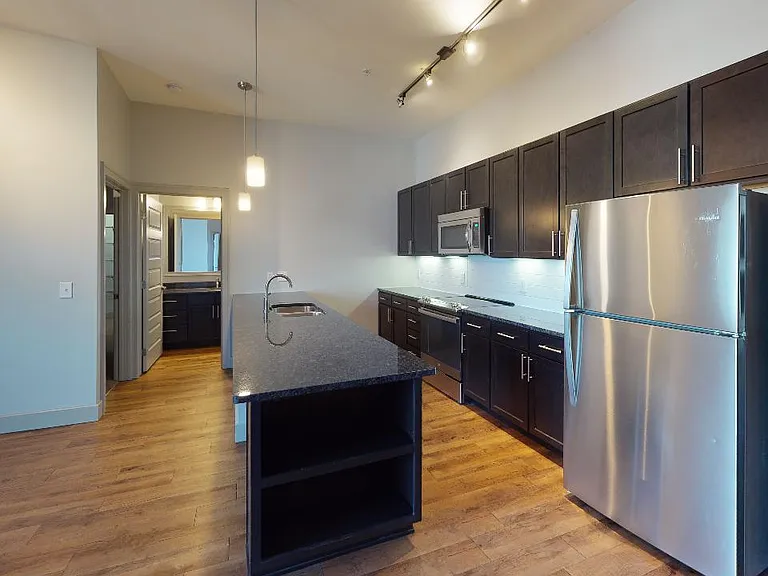 Apartment kitchen with stainless steel appliances, dining and living room with wood-style flooring.