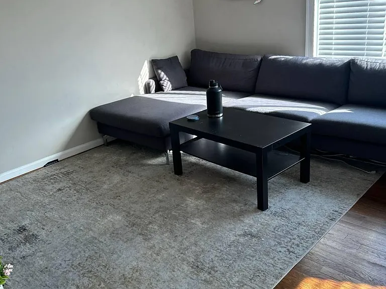 Living room with a sectional sofa, coffee table, and large window with blinds for natural light and comfortable lounging.