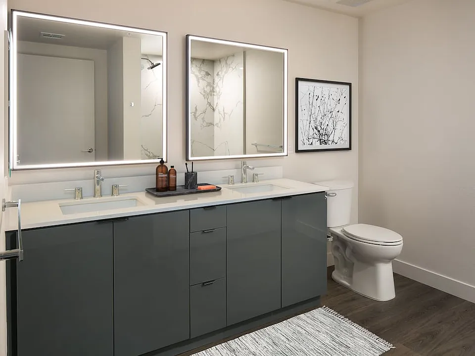 Upgrade Package Bath with grey cabinetry, white quartz countertop, marble shower surround, and lit vanity mirror