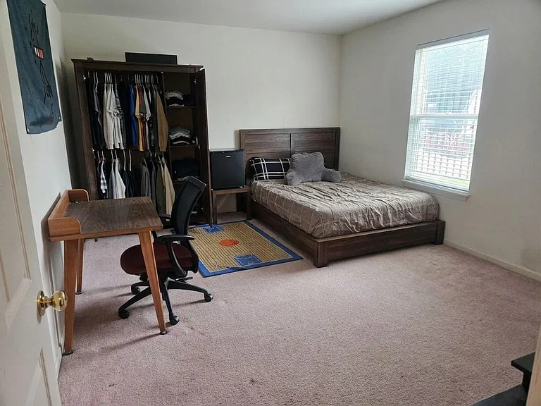 Furnished bedroom with queen bed, desk workspace, wardrobe storage, and a large window for natural light.