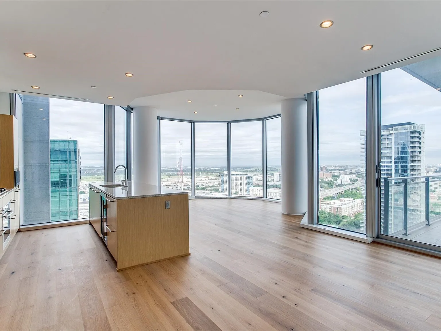 Open-concept living space with expansive floor-to-ceiling windows, wood-finish flooring, recessed lighting, and a kitchen island with a stainless steel sink