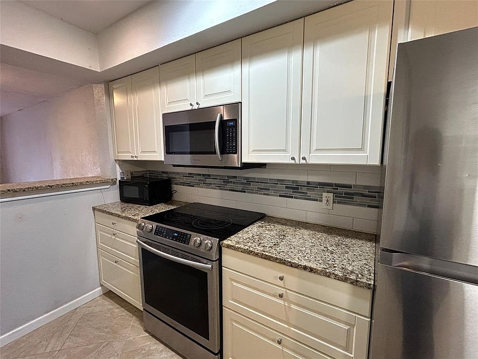 Kitchen with appliances with stainless steel finishes, light stone counters, and white cabinets