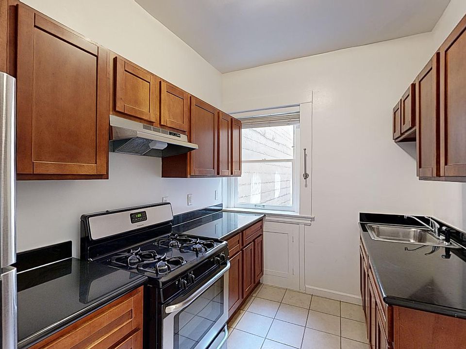 Modern kitchen with stainless steel appliances, countertops, and wooden cabinets, featuring a window for natural light.
