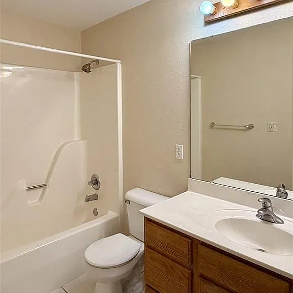 Bathroom featuring a built-in tub and shower combination, a vanity with a white countertop and wood-finish cabinetry, and white tile flooring