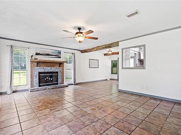 Unfurnished living room with tile flooring, ceiling fan, a fireplace, and crown molding