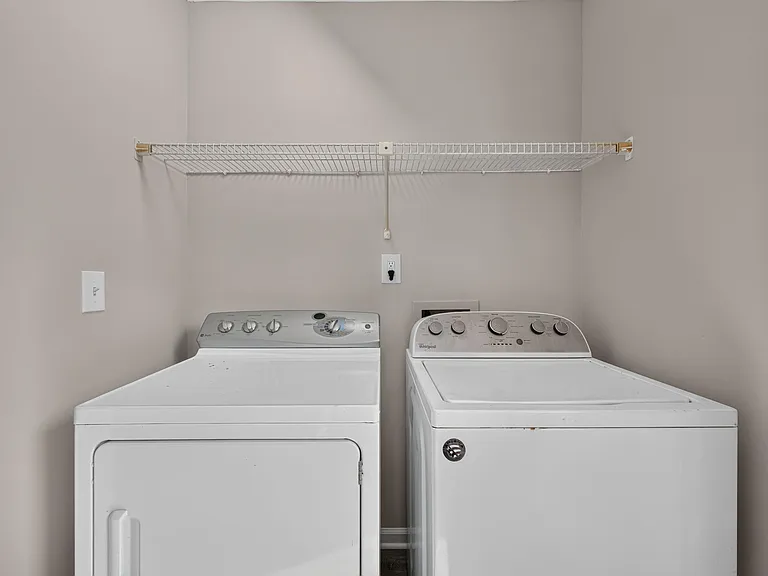 Dedicated laundry nook with side-by-side washer and dryer and a wire shelf for convenient storage.