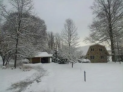 Snow-covered Dutch-style stone home with a long driveway and trees creating a serene winter landscape.