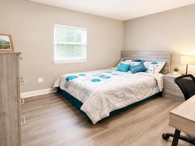 Furnished bedroom with a full/queen bed, nightstand lighting, dresser storage, and a dedicated desk workspace.