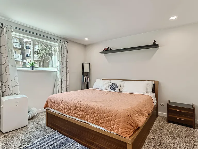 Spacious bedroom with a comfortable bed, nightstand, and a large window with curtains for natural light and privacy.