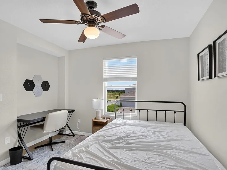 Private bedroom featuring a ceiling fan, window with blinds, and a dedicated desk/workspace plus nightstand storage.