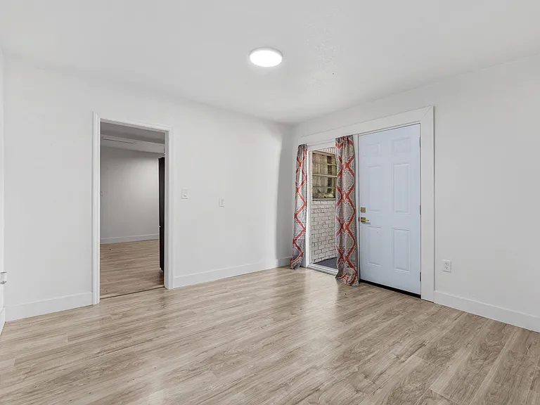 Open main living area with durable wood-look flooring, overhead lighting, and direct access to the entry and adjacent rooms.