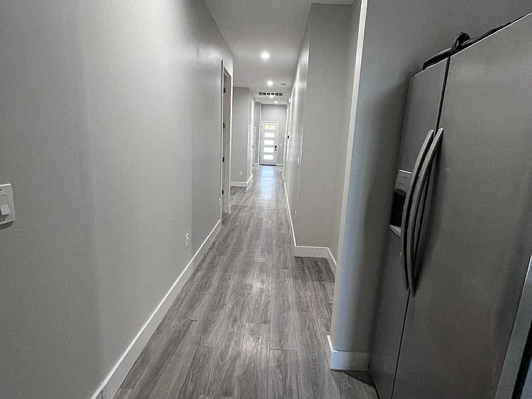 Long hallway with durable wood-look flooring and recessed lighting, connecting bedrooms and common areas to the entry.