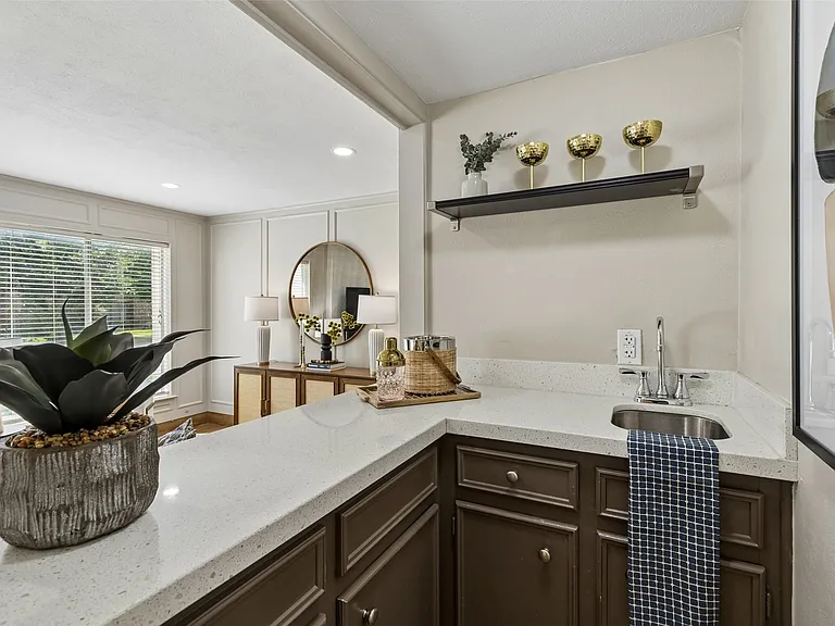 Wet bar featuring a stainless steel sink, quartz-finish countertop, dark wood-finish cabinetry, and an open display shelf