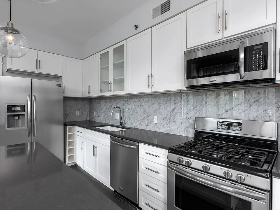 York House designer kitchen with gas stove, quartz countertops, stainless steel appliances, marble kitchen backsplash, and slate tile floor.