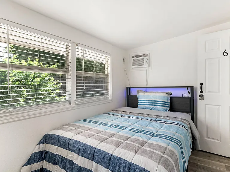 Private bedroom with large windows, blinds, and a comfortable bed setup with easy access to in-room AC.