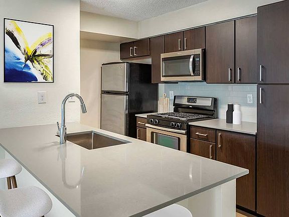 Finish Package III kitchen with espresso cabinetry, grey quartz countertops, stainless steel appliances, tile backsplash, and hard surface flooring