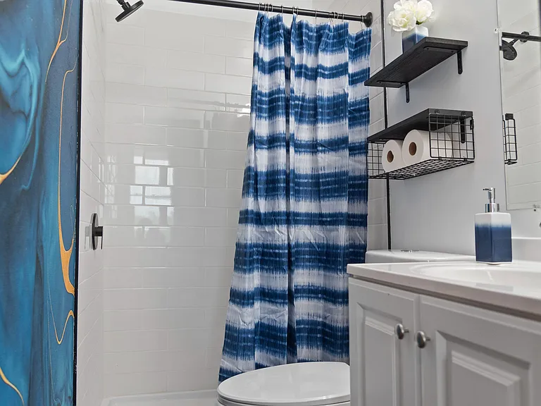 Bathroom features a tiled tub/shower combo, vanity sink, and wall shelving for convenient everyday storage.