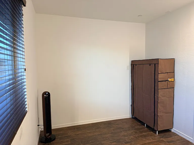 Versatile room with a large window and wood-look flooring, offering space for a bed setup plus wardrobe/storage.