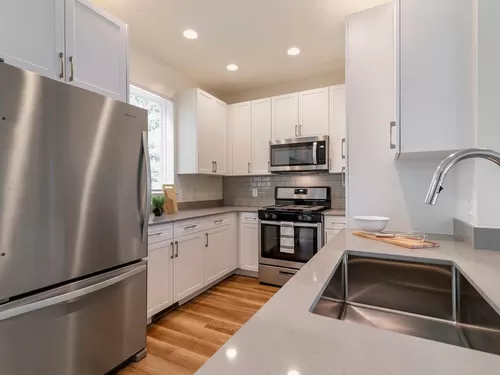 Renovated Package II kitchen with white cabinetry, grey quartz countertops, grey subway tile backsplash, stainless steel appliances, and hard surface flooring - Avalon Northborough