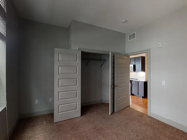 Spacious apartment bedroom with large closet and plush carpet flooring.