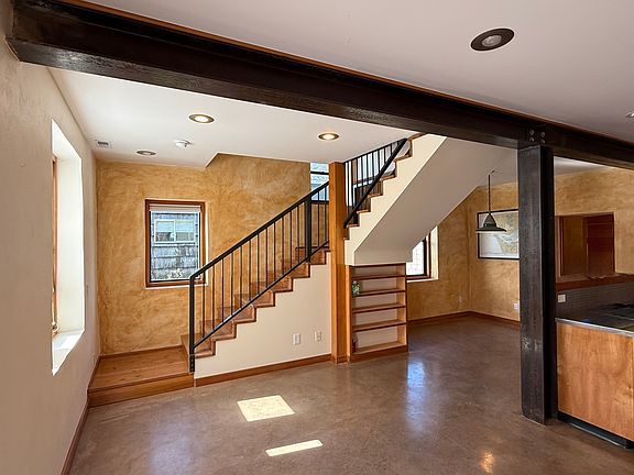 Main living room with custom steel beam, plaster walls, heated concrete floors, plenty of natural light, built-ins, storage under stairs, dimmable can lights let you control the vibe.