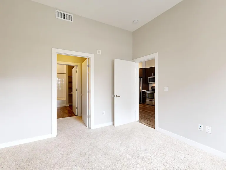 Spacious apartment bedroom with large closet, attached bathroom, and plush carpet flooring.