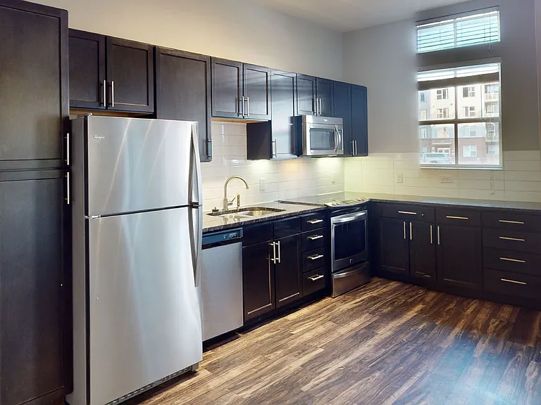 Apartment kitchen with stainless steel appliances, granite countertops and wood-style flooring.