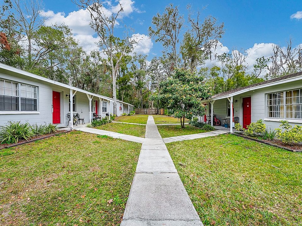 Quaint courtyard view with charming single-story apartments featuring vibrant red doors and lush greenery, perfect for tranquil living.