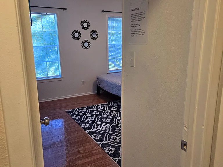 Bedroom with two windows, wood-style flooring, and space for a bed and essentials, accented by wall decor and an area rug.