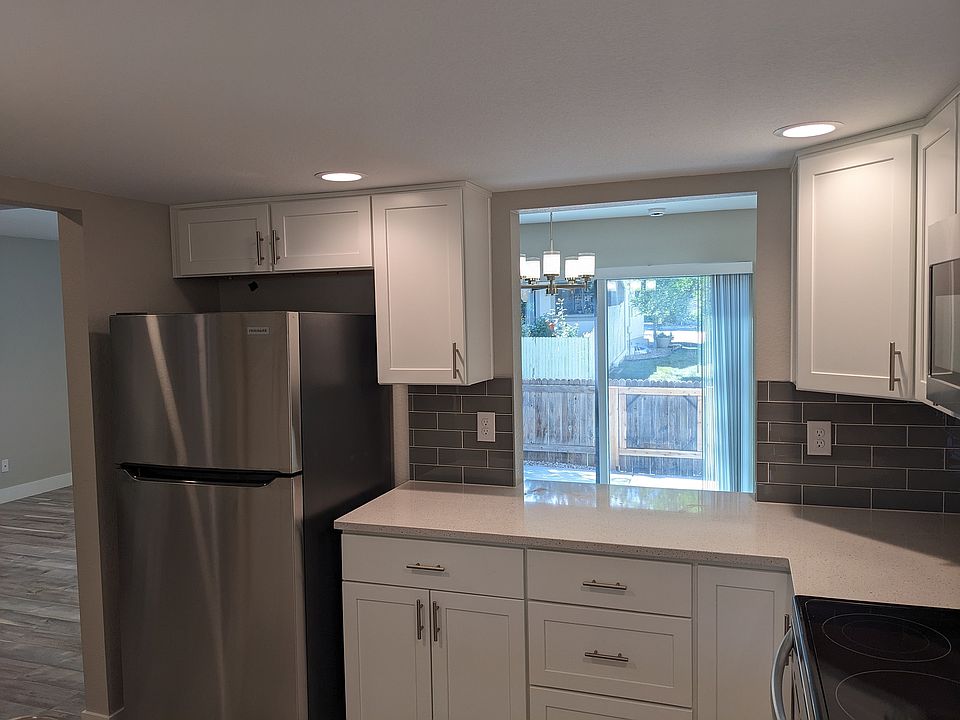 Contemporary kitchen with sleek stainless steel appliances, elegant white cabinetry, and a bright dining area overlooking a lush backyard.