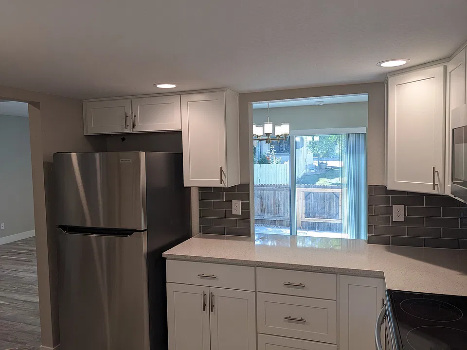 Contemporary kitchen with sleek stainless steel appliances, elegant white cabinetry, and a bright dining area overlooking a lush backyard.