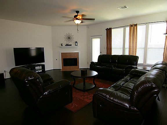 Light and bright large living room with dark wood flooring, a gas log fireplace and upgraded ceiling fan with energy efficient light bulbs