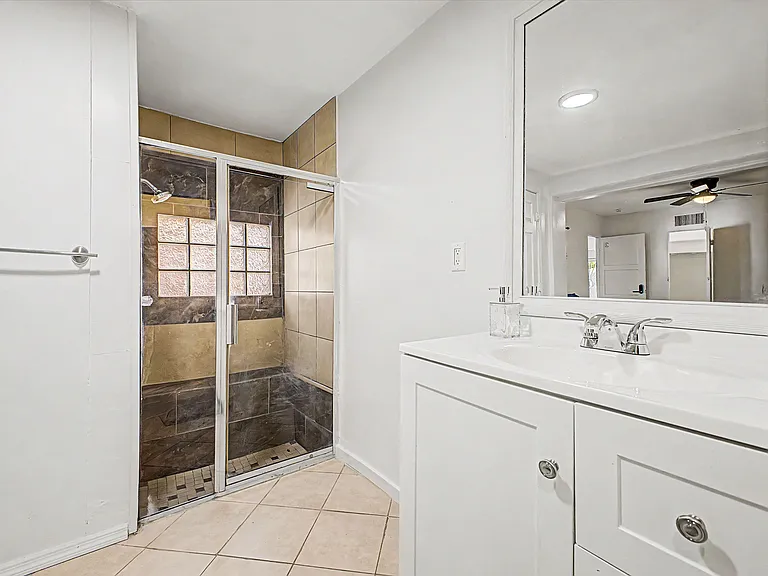 Full bathroom with a tiled, glass-enclosed shower, large vanity with storage, and an oversized mirror for daily routines.