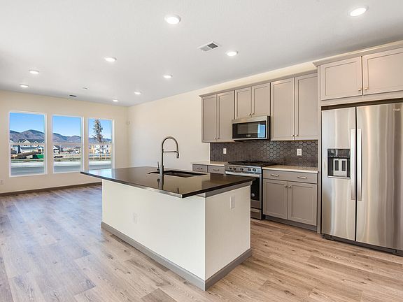 A modern, open-concept kitchen with gray cabinets, stainless steel appliances, and a large window ov