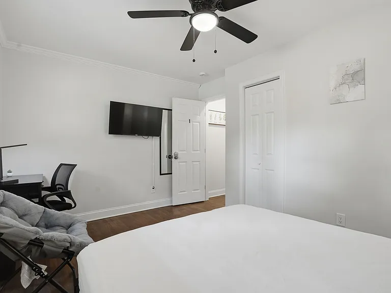 Private bedroom with hardwood floors, ceiling fan, wall-mounted TV, desk workspace, and a closet for convenient storage.
